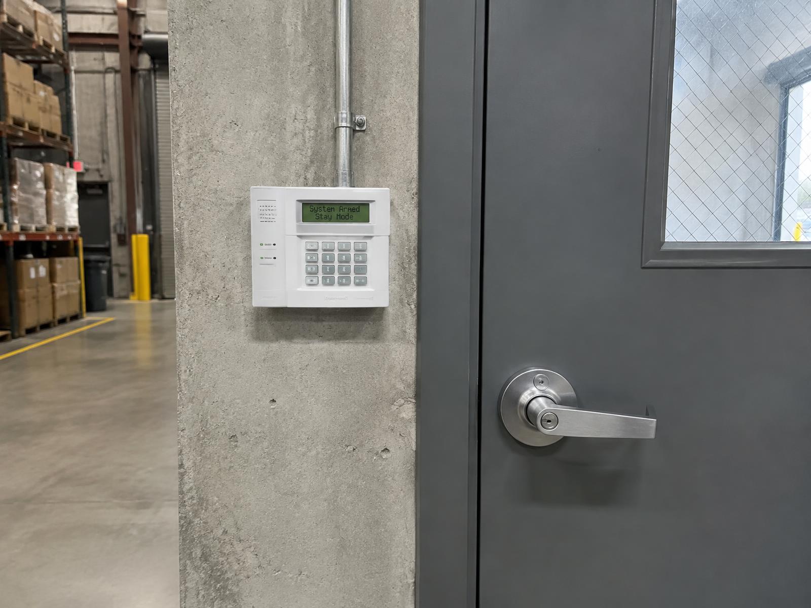 Commercial alarm keypad mounted beside a steel back-entrance door in a warehouse